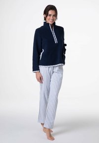 Maglione in pile blu navy con mezza cerniera, piping bianco e tasche frontali, abbinato a pantaloni del pigiama a righe bianche e azzurre.