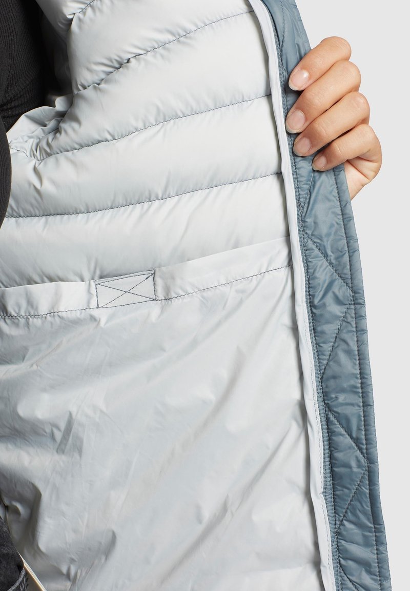 Leichte Steppjacke mit schimmerndem silbernen Innenfutter und blauer Außenschale, mit gesteppten Abschnitten und einer versteckten Tasche.