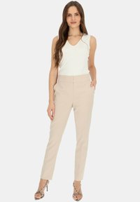 Beżowe dopasowane spodnie o wysokim stanie, z bocznymi kieszeniami i smukłą sylwetką, w zestawie z dopasowaną białą koszulką bez rękawów.