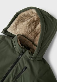 Giacca isolata verde con cappuccio foderato in morbido pile beige e zip frontale. Presenta una tasca sul petto con zip orizzontale.
