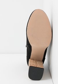 Talons en daim noir avec une semelle en liège, semelle en caoutchouc texturé et un bout arrondi lisse avec des détails de couture minimaux.