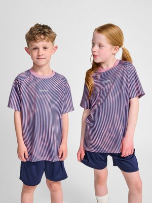 To børn iført matchende lilla og pink stribede sportstrøjer og marineblå shorts står mod en ensfarvet baggrund.