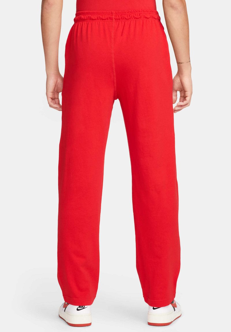 Czerwone dresowe spodnie z elastycznym pasem, prostymi nogawkami, gładkiego bawełnianego materiału i mankietami w kostkach, w połączeniu z białymi trampkami.