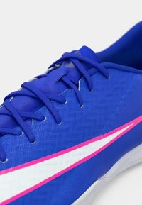 Μπλε αθλητικό παπούτσι με υφασμένο άνω μέρος, αντίθετες ροζ και λευκές λεπτομέρειες και κορδόνια περασμένα μέσα από τις οπές.