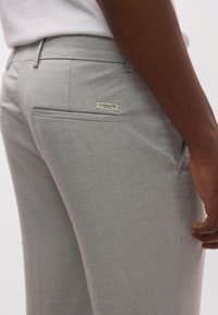 Ανοιχτό γκρι παντελόνι ραμμένο με υφή υφάσματος, διαθέτει πίσω τσέπη και μικρή ετικέτα με το όνομα της μάρκας.