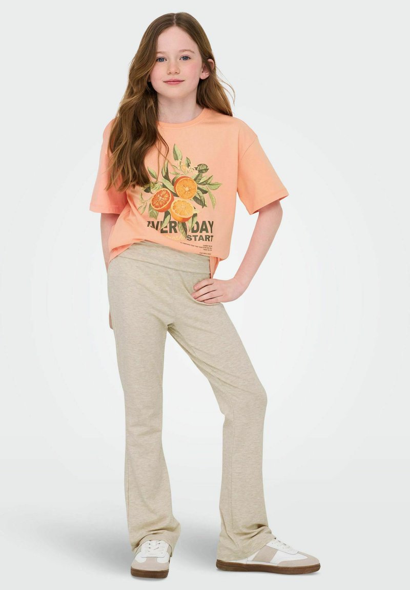 Perziken graphic t-shirt met een print van sinaasappels; beige flare broek; witte en beige sneakers; gladde stoftextuur; casual pasvorm.