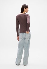 Top maro cu maneci lungi si ajustat, asortat cu blugi lejeri, de culoare bleu deschis, cu talie inalta, avand o croiala dreapta si detalii usor decolorate.