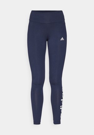 Tamsiai mėlynos sportinės legging'os su aukštu juosmeniu, pagamintos iš tamprių medžiagų. Kairėje kojoje yra baltas prekės ženklas.