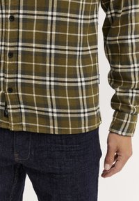 Grøn- og hvidternet flannel-skjorte med sorte knapper, lange ærmer og lige kant. Matches med marineblå jeans.