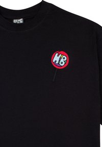 Čierne bavlnené tričko s dlhým rukávom, na ktorom je na ľavej hrudi vyšitý malý farebný logo cukríka.