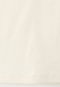 Prim-plan al unui material crem cu dungi verticale texturate și tiv cusut în partea de jos.