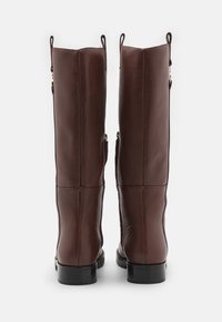 Brown leather knee-high boots with a smooth texture, side zippers, and flat black soles. Reinforced seams and pull tabs at the top.