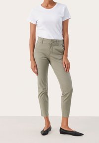 Pantalons kaki ajustés, avec une taille mi-haute, des poches latérales et des détails cousus. Associés à un t-shirt blanc basique et des ballerines noires.