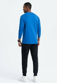 Blauwe langwerpige shirt met lange mouwen, zwarte joggers, witte sneakers. Glad stof, losse pasvorm, eenvoudig ontwerp, geen zichtbare patronen of accenten.