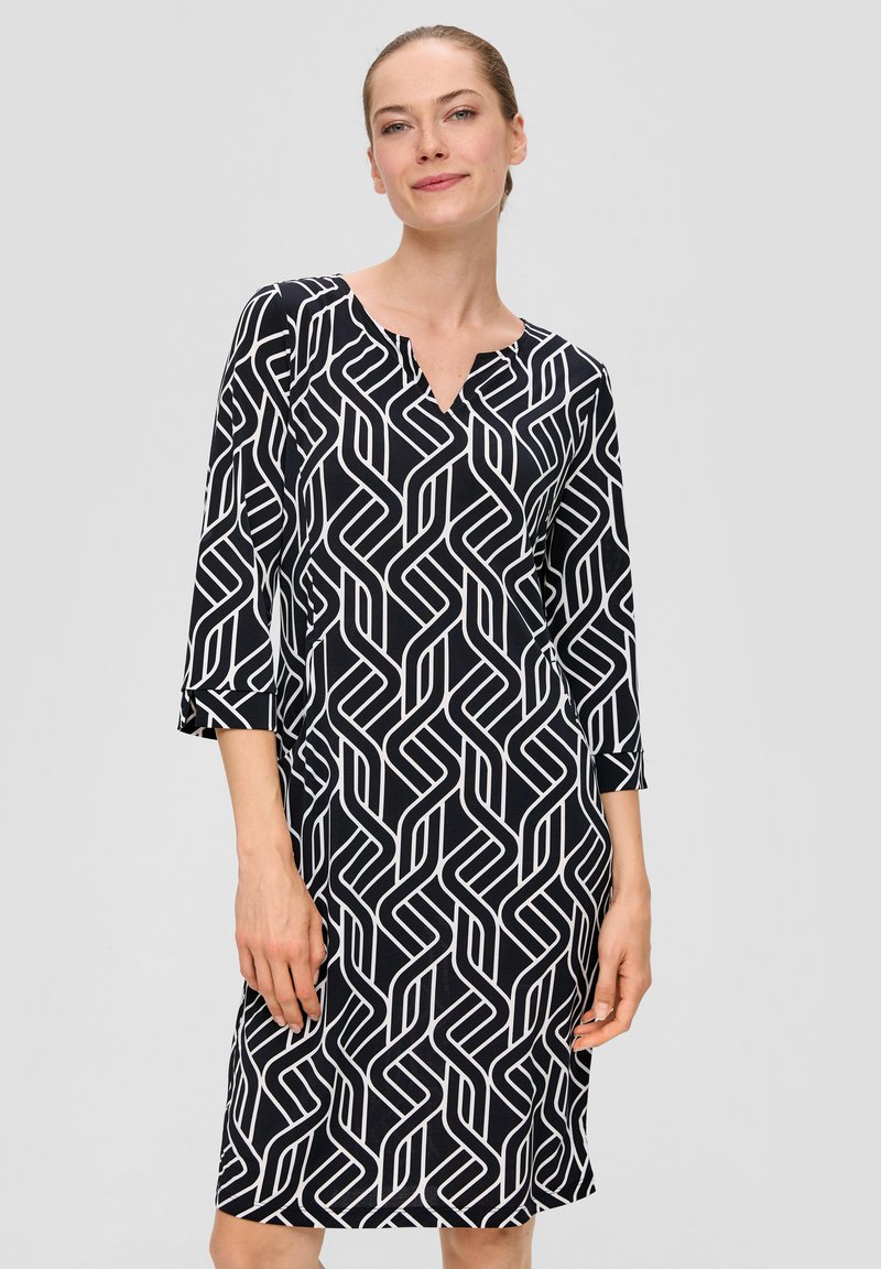 Robe à motifs noir et blanc avec un décolleté en V, des manches trois-quarts et un design géométrique comportant des lignes entrelacées. Texture de tissu douce.