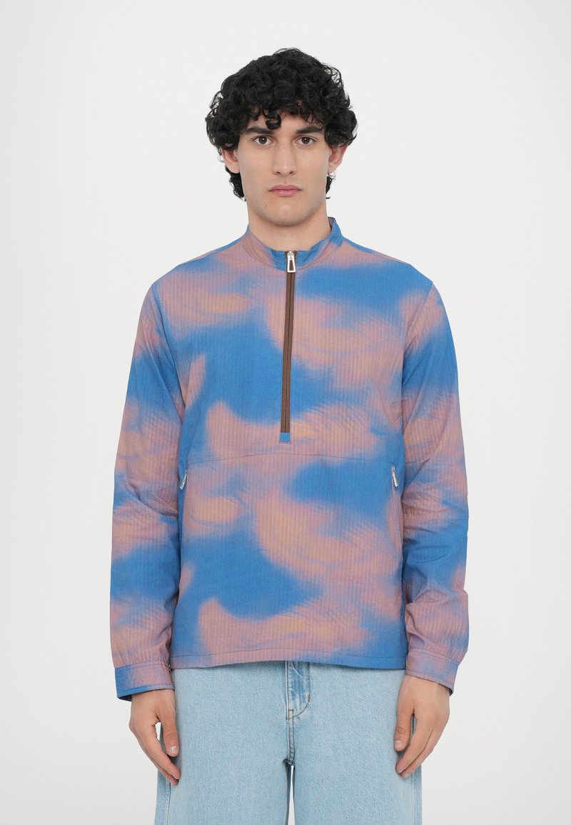 Lightweight pullover in blue and coral tie-dye pattern, featuring a mock neck, half-zip front, and ribbed texture. Long sleeves and side pockets.