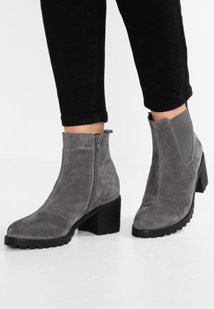 Bottines en suède gris avec une fermeture éclair sur le côté, des accents élastiques et un chunky talon noir. La semelle texturée offre une traction pour la stabilité.