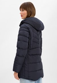 Granatowa kurtka puchowa, izolowana z detalami szycia. Posiada kaptur, zamek błyskawiczny oraz nieco wydłużony tył dla większego ciepła.