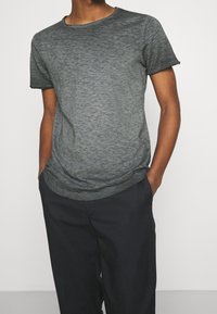 Camiseta de manga corta gris oscuro, con una tela ligeramente texturizada y escote redondo, combinada con pantalones negros; ajuste casual.