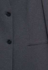 Gros plan sur le tissu gris foncé d'une veste de costume avec deux boutons noirs et une poche à fente horizontale sur le côté droit.