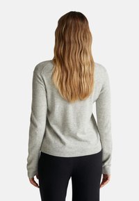 Šedý pletený svetr s dlouhými rukávy a žebrovaným lemem, zobrazený zezadu, zdůrazňující jemnou texturu a decentní design. Předváděn s černými kalhotami.