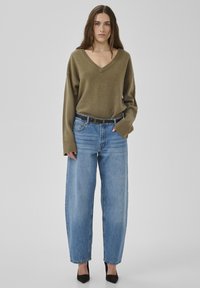 Pull vert olive à col en V avec poignets côtelés, associé à un jean bleu à jambes larges et des escarpins noirs pointus. Design simple et décontracté avec une coupe ample.