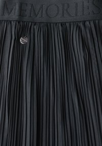Black pleated skirt with a textured waistband featuring the word "MEMORIES" embossed. A silver button detail is visible at the waist.
