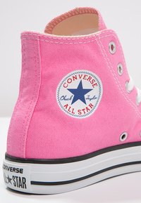 Rosa kanvas høyhælte sneakers med hvite øyer og snøring, med en rund blå og rød All Star-logo på den ytre hælen.