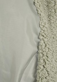 Miękka, jasnoszara gładka tkanina obok grubego, teksturowanego, kędzierzawego płaszcza z ecru, pokazująca kontrastujące powierzchnie tekstylne obok siebie.