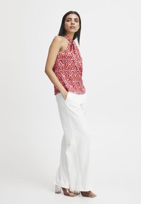 Top halter a righe rosse e bianche con collo annodabile, abbinato a pantaloni bianchi a gamba larga e sandali con tacco trasparente. Tessuto dalla texture liscia.