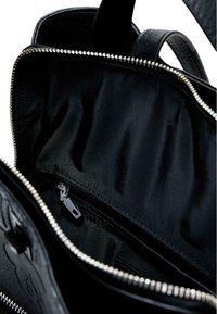 Schwarze Handtasche mit Innenansicht, die eine Reißverschlusstasche mit einem silbernen Reißverschlussgriff und glatter Stoffauskleidung zeigt.