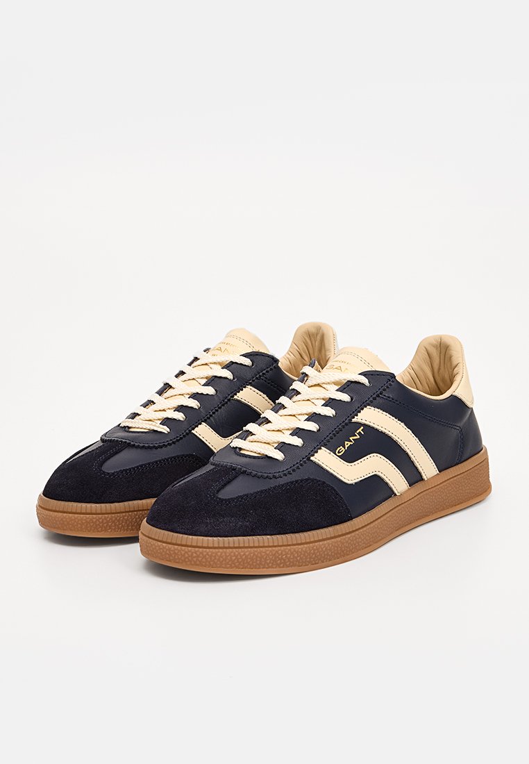 Marineblaue Sneaker aus Wildleder und Leder, mit cremefarbenen Akzenten, runder Zehenpartie, robuster Gummisohle und kontrastierenden Streifen an den Seiten.