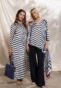 Deux femmes portant des vêtements en tissu rayé bleu marine et blanc. L'une porte une longue robe ; l'autre un haut ample avec un pantalon noir et des accessoires.