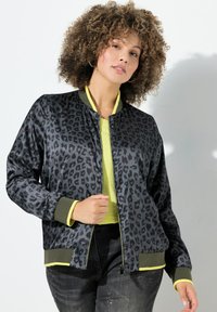 Leopardmönstrad bomberjacka i svart och grått med en gul insida, ribbade ärmslut och nederkant. Kombinerad med en ljusgul topp och mörka jeans.