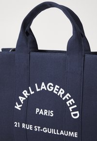 Navy canvas tote bag with dual handles, featuring white printed text reading "KARL LAGERFELD PARIS 21 RUE ST-GUILLAUME." Smooth texture.