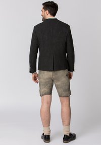 Dunkelgrauer Wollblazer mit Reverskragen und zwei Knöpfen, kombiniert mit beigen Leder-Shorts mit genähten Details und Seitentaschen.