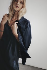 Marinblå satinblus med lång, avslappnad passform, utrustad med spetsig krage och knappar, bärs över en matchande ärmlös klänning.