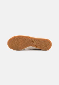 Suela de una zapatilla de color claro con una suela de goma que presenta un diseño de patrones circulares y la marca "RC42".