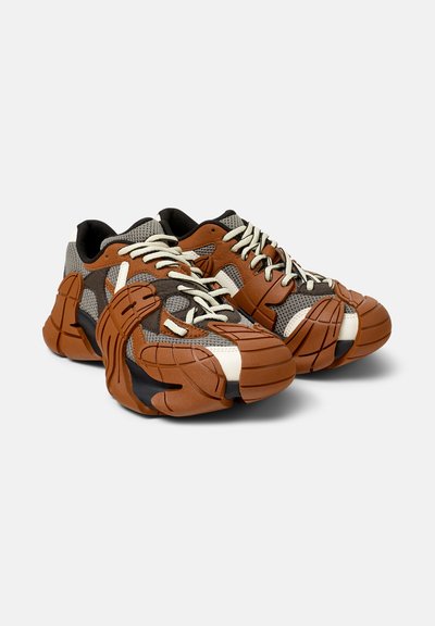 Sneaker mit einer braunen und schwarzen Gummisohle, grauem Mesh-Obermaterial und cremefarbenen Schnürsenkeln. Auffälliges strukturiertes Design mit geschichteten Akzenten.