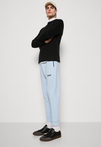 Light blue sweatpants with black "BOSS" logo, paired with a black sweater and black sneakers. Model wears a beige cap and white socks.
