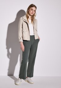 Veste en suédine beige avec boutons-pression, chemise blanche, pantalon vert ajusté et baskets crème. Textures lisses et design contemporain.