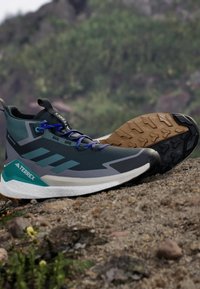 Graue und türkisfarbene Wanderschuhe mit einem Obermaterial aus Mesh, Gummisohle und blauen Schnürsenkeln. Sie verfügen über ein Design mit drei Streifen an der Seite und einem robusten Profilmuster.