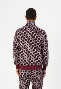 Chaqueta de franjas color burdeos y marino hecha de un tejido suave, con un cuello alto, puños acanalados y un diseño a juego en los pantalones.