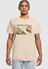 Beige cotton t-shirt featuring a graphic print of Michelangelo's artwork. Round neck, short sleeves, and relaxed fit.