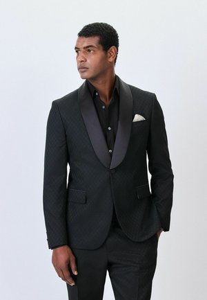 Schwarze Smokingjacke mit satinierter Reversklappe, strukturiertem Stoff im Diamantmuster, einzelnem Knopfverschluss und einem weißen Taschentuch.