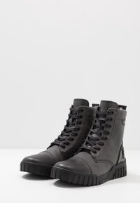 Botas altas de cuero negro con suelas de goma gruesas, cordones frontales y cuellos acolchados, colocadas sobre un fondo blanco liso.