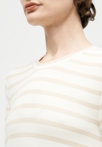 Nahaufnahme einer Person, die ein weißes T-Shirt mit leicht beigefarbenen horizontalen Streifen trägt.