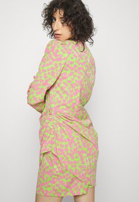 Vestido justo em tecido verde vibrante com padrões de corações cor-de-rosa, costas franzidas e detalhes em botão ao longo do lado.