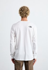 Weißes langärmliges T-Shirt aus Baumwolle, mit einem kleinen schwarzen Logo auf dem oberen Rücken. Einfacher, lässiger Schnitt mit rundem Halsausschnitt.