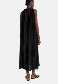 Czarna, bezrękawnikowa sukienka z pionowymi metalicznymi paskami, luźny krój, długość do połowy łydki oraz detal z marszczeniem przy dekolcie. Uzupełniona czarnymi sandałami.